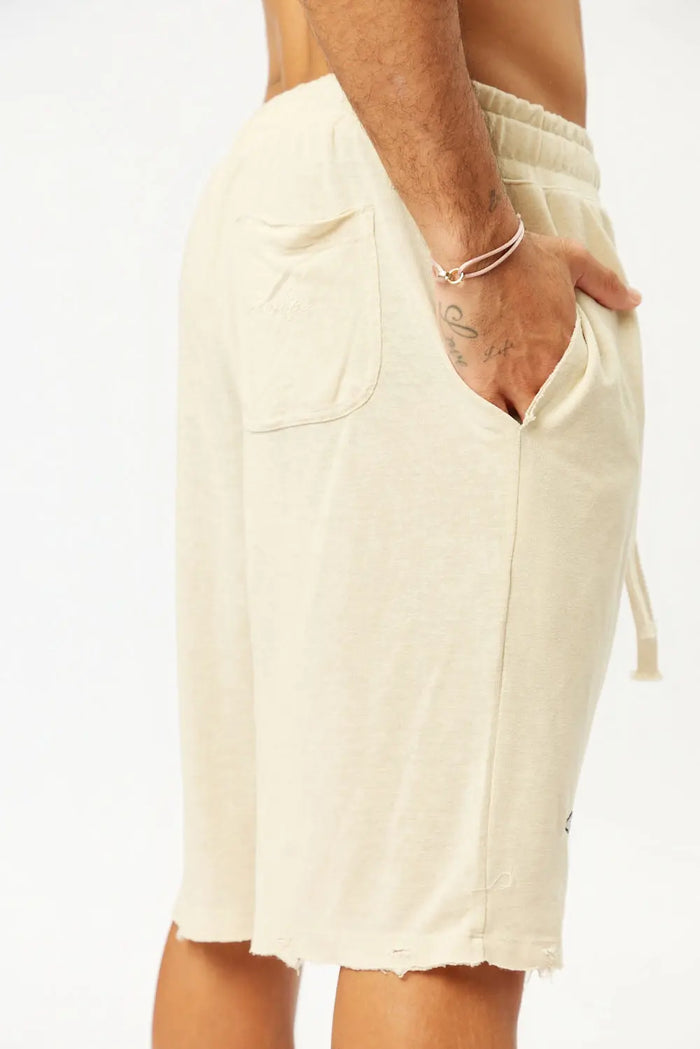 Base Shorts in Stone, close up of the shorts on a person, showing the pocket, drawstring, and distressed hem