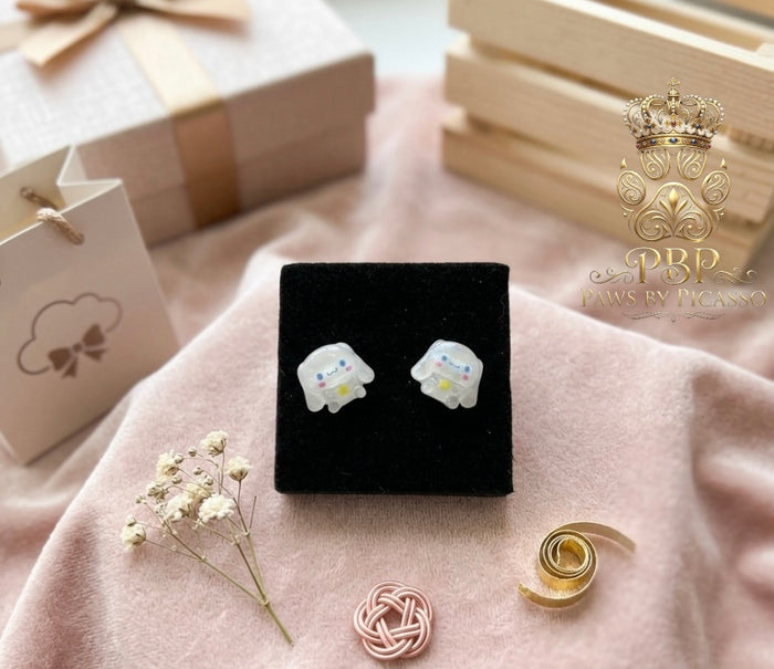 Pair of animal-shaped earrings on a black display card with decorative elements on a pink fabric background.
