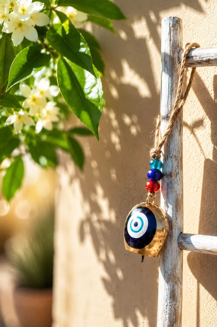 Single Hanging Bell Mobile with a blue evil eye design, red and blue beads, hanging from a rustic white ladder