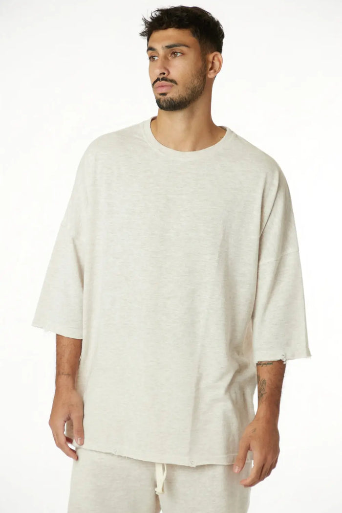 Man wearing a 3/4 Sleeve Nicki Soft in Melange Stone, a light beige oversized t-shirt with raw edges and matching shorts