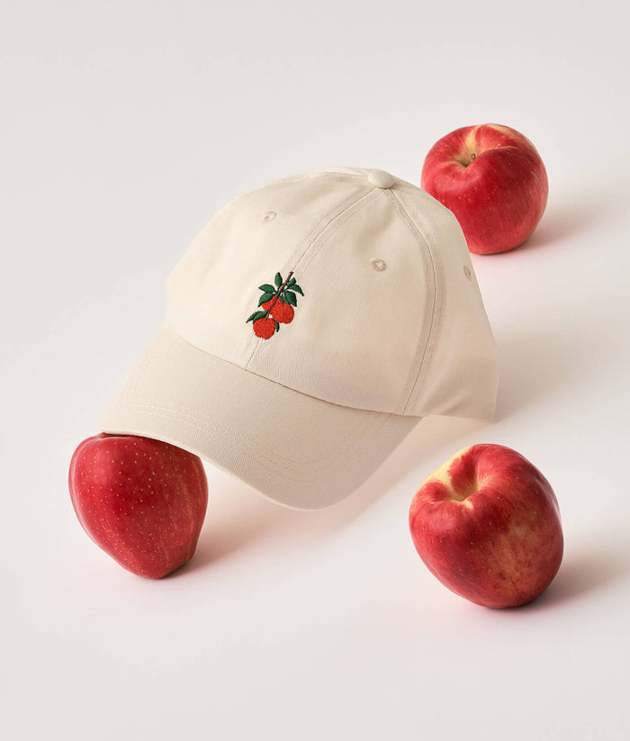 Beige cap with apple design surrounded by red apples on a light background