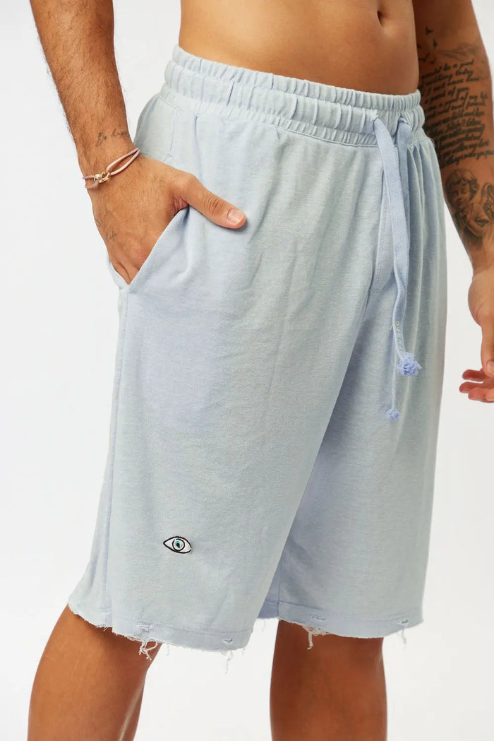 BASE Shorts in light blue with an eye logo and distressed hem, worn by a person with a hand in the pocket