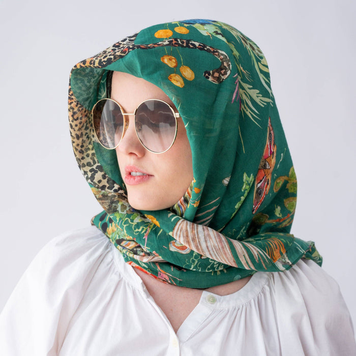 Person wearing a green patterned headscarf and sunglasses on a white background