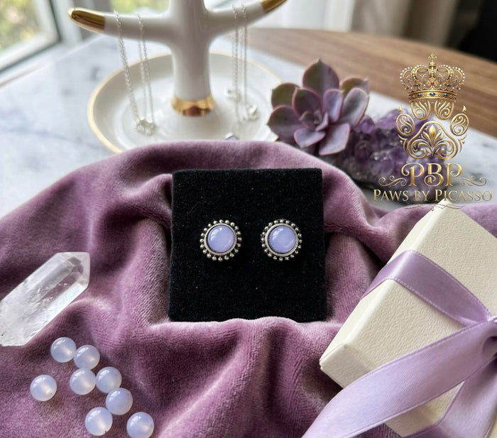 Pair of earrings on a black display card with a purple cloth and decorative elements.