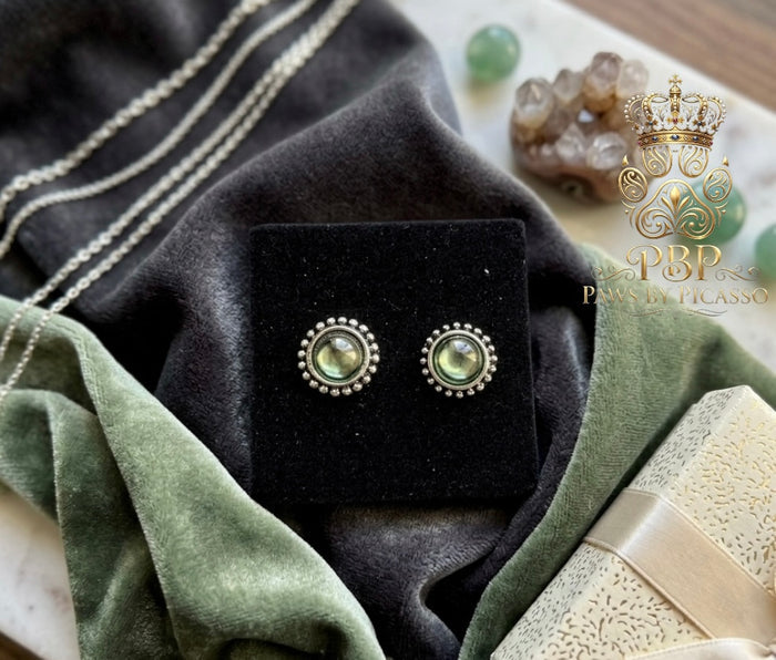Pair of green gemstone earrings on a black velvet stand with a decorative background.