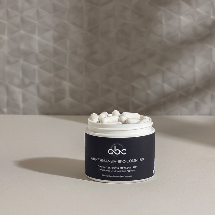 Open jar of InfiniWell Akkermansia-BPC Complex supplement filled with white capsules on a neutral tabletop.
