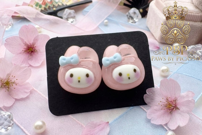 Pink animal-shaped earrings on a black card with cherry blossoms and pearls in the background.
