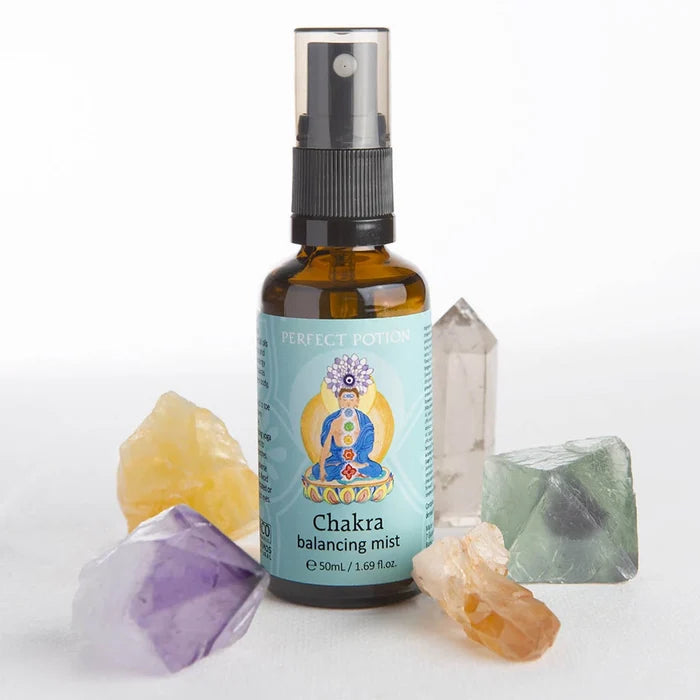 A 50ml amber glass spray bottle of Perfect Potion Chakra Balancing Mist, surrounded by various raw crystal points on a white background.