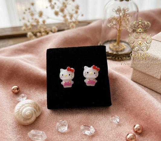 Cartoon cat earrings on a black stand with decorative elements on a pink surface