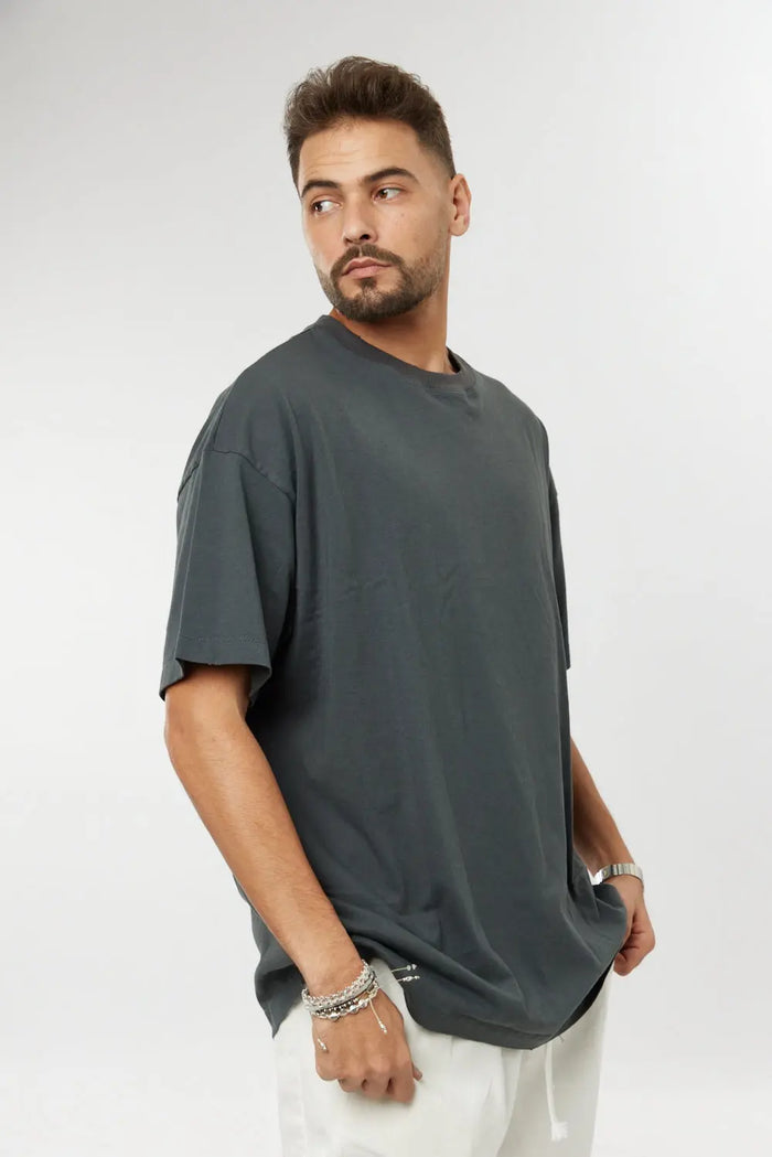 Man wearing a grey cotton t-shirt and white trousers, looking over his right shoulder