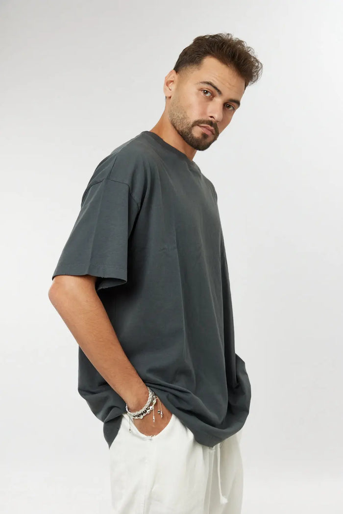 Man wearing a grey cotton t-shirt and white trousers, with a hand in his pocket