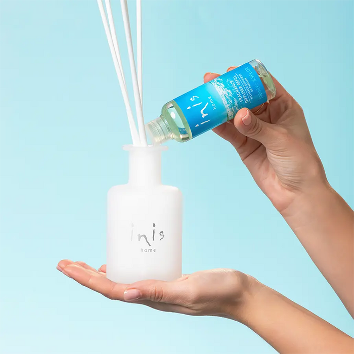 Person pouring a blue liquid of diffuser into a white jar against a light blue background