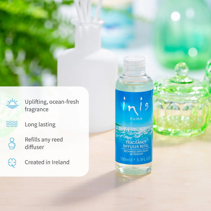 Clear bottle of 'inis home' fragrance diffuser refill on a wooden surface with blurred greenery in the background.
