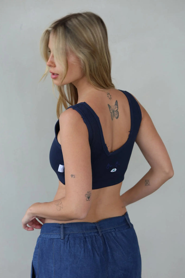 Blonde woman wearing a navy blue Essential Crop Top and blue jeans, facing away from the camera with her head turned to the left