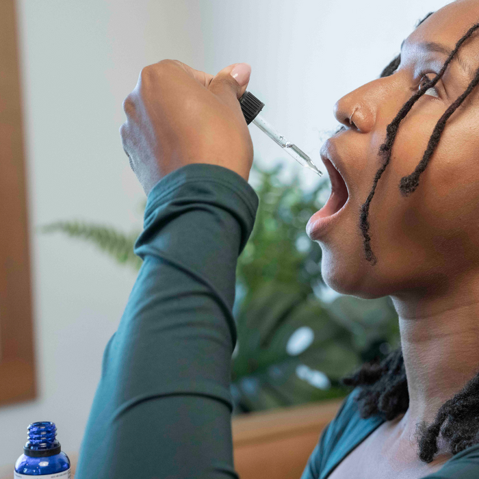 Person tilting head back and using a dropper to place Focus More supplement drops into their mouth in a bright indoor setting