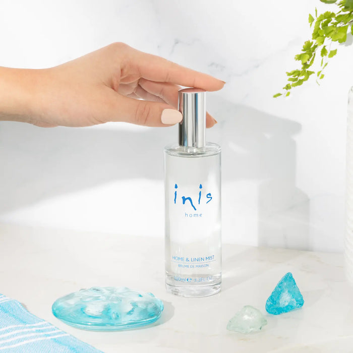 Hand holding a clear spray bottle labeled 'inis' with blue text on a light background.