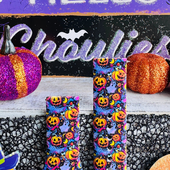 Both halves of the Jack-O-Lantern Jive Samsung Galaxy Watch band standing upright between orange and purple glitter pumpkins.