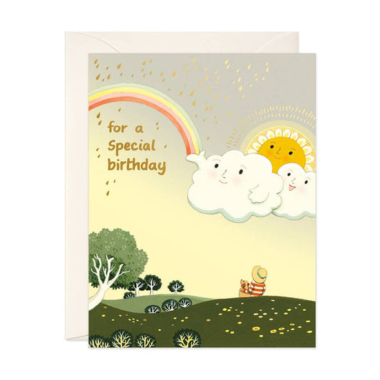 Children's birthday card with a rainbow, clouds, and a bear in a field.