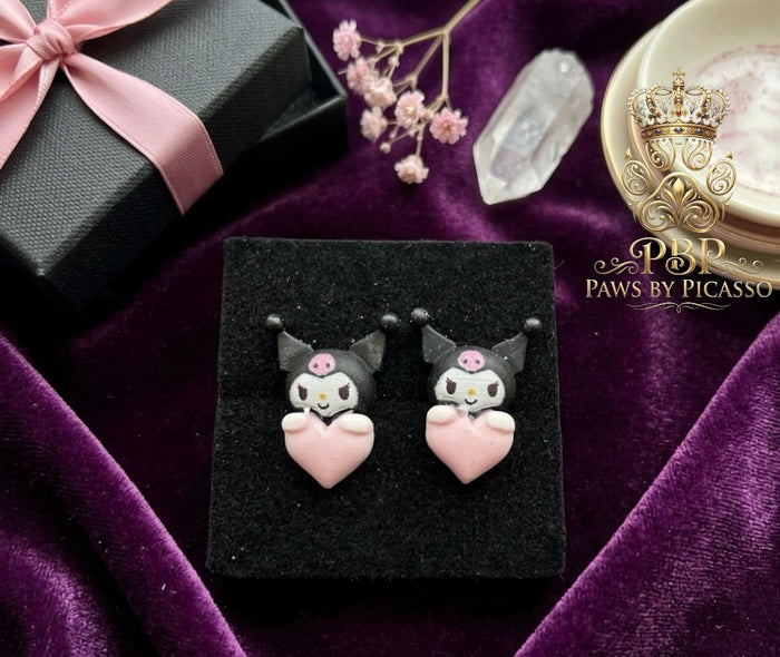 Pair of cat-shaped earrings on a black card with 'Paws by Picasso' branding, set against a purple fabric background.
