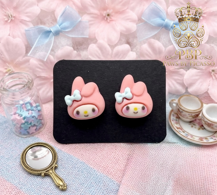Pink cartoon-style earrings on a black card with decorative background