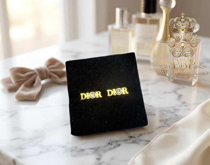 Dior earrings on a marble surface with perfume bottles in the background