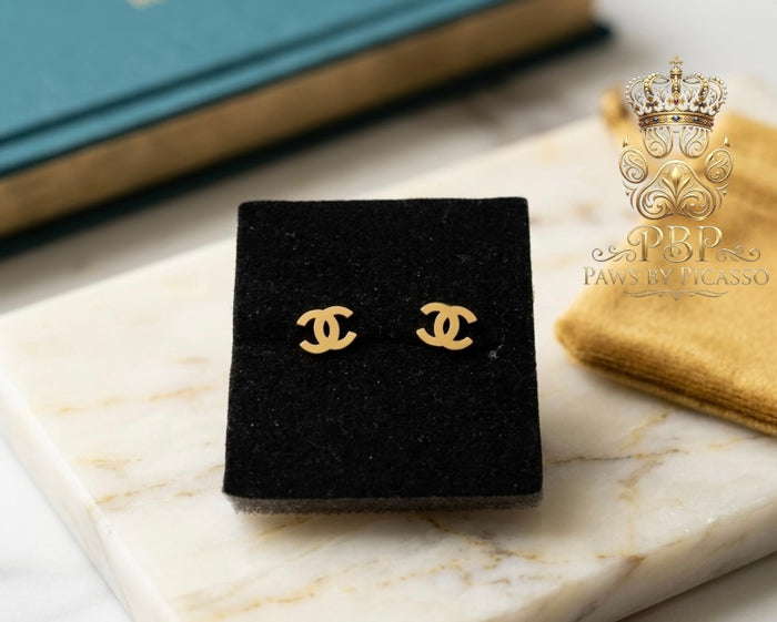 Gold earrings on a black display stand with 'Paws by Picasso' branding in the corner.