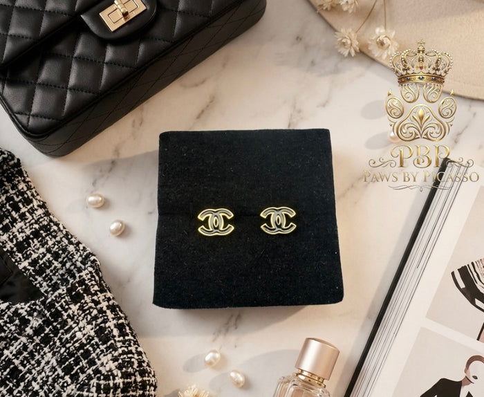 Gold earrings on a black display box with a marble background, Chanel handbag, and perfume bottle.