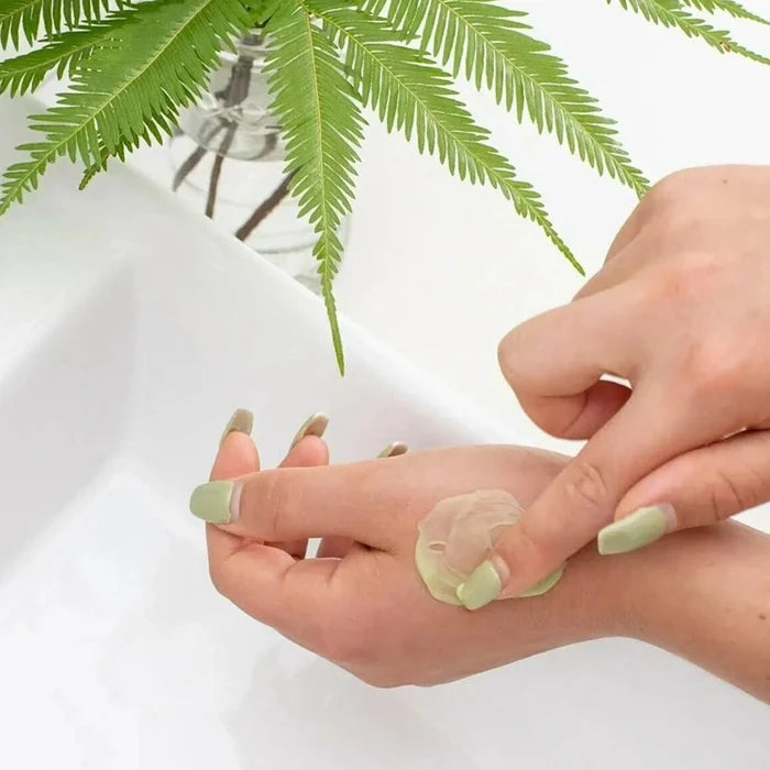 Person applying light green antifungal skin cream to their hand with a fern in the background
