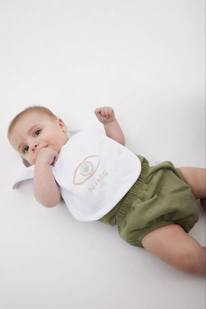 Newborn Cotton Bib with an eye graphic and Safe & Protected text, worn by a baby in green shorts