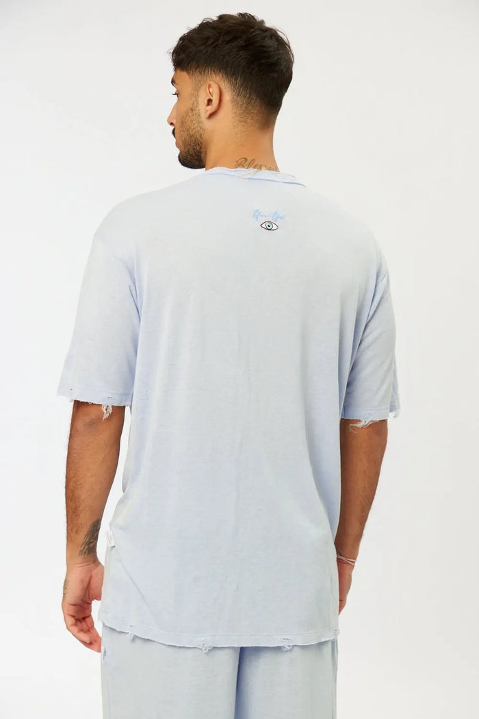 Back of Nicki Soft Open Top in light blue, with distressed details on sleeves and hem, and a small eye graphic on the upper back