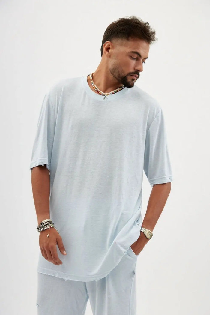 Man wearing a TFU Soft Essential Tee in sky blue with a beaded necklace and bracelets