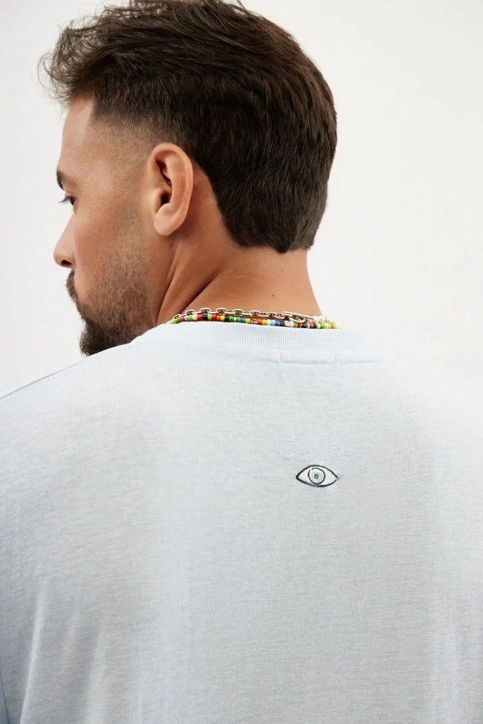 Back of a man wearing a sky blue TFU Soft Essential Tee with a small eye graphic and TFU logo embroidered on the upper back