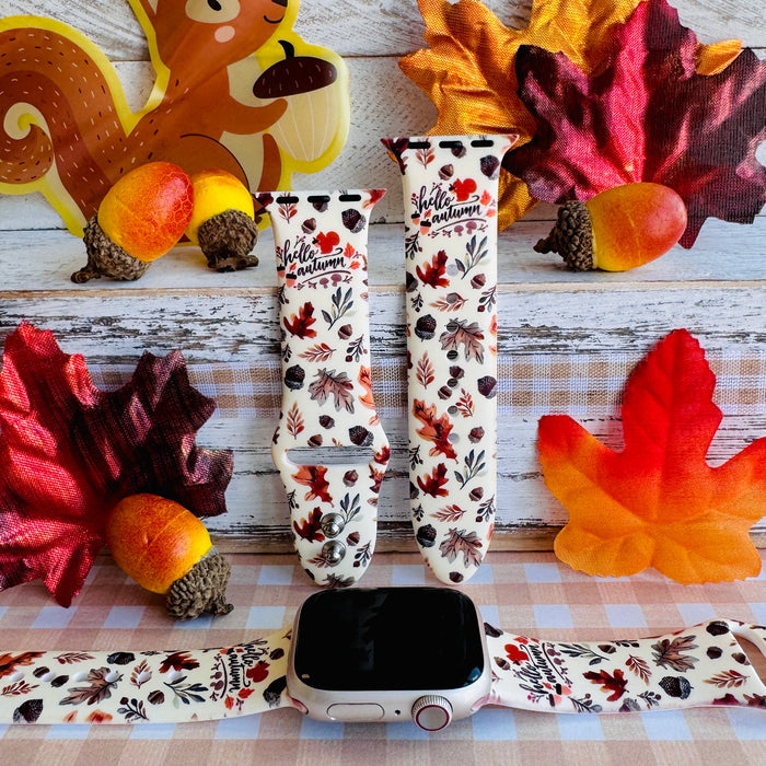 Nutty For Fall silicone Apple Watch band shown with an Apple Watch, both strap halves standing upright to display the cream base with watercolor acorns, oak leaves, and hello autumn script.