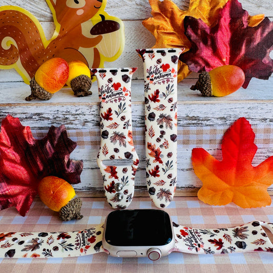 Nutty For Fall silicone Apple Watch band shown with an Apple Watch, both strap halves standing upright to display the cream base with watercolor acorns, oak leaves, and hello autumn script.
