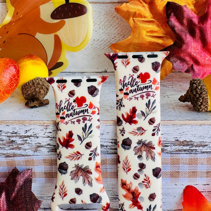 Nutty For Fall Apple Watch band front view of both strap halves against a squirrel and autumn leaf backdrop, showing the hello autumn lettering and acorn print.
