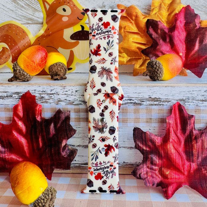 Nutty For Fall Apple Watch band single strap half standing on weathered wood, showing the cream silicone with rust and burgundy oak leaves and scattered acorns.