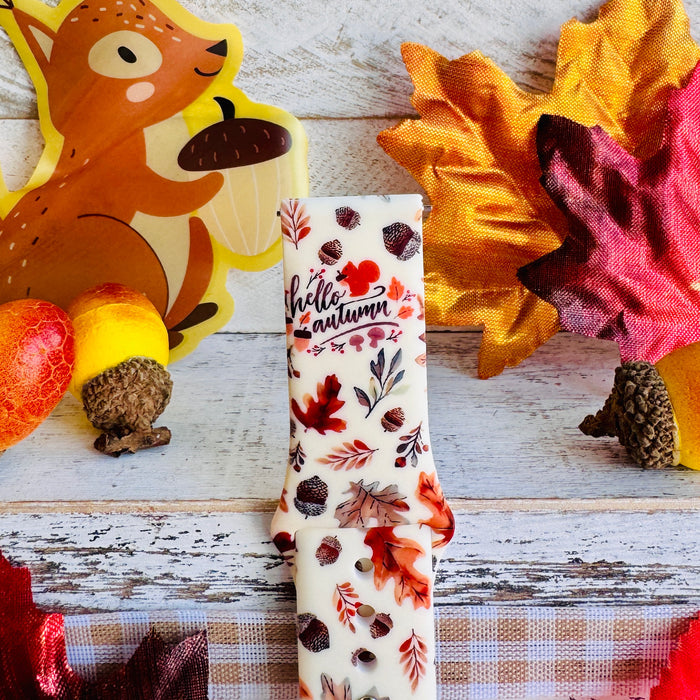 Nutty For Fall Samsung Galaxy Watch band single strap half standing on weathered wood, showing the cream silicone with rust and burgundy oak leaves and scattered acorns.