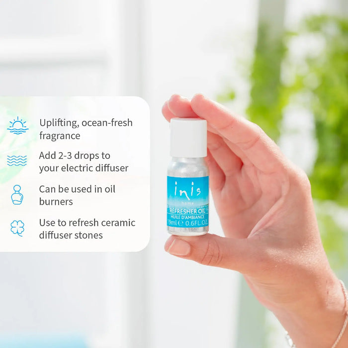 Hand holding a small bottle of 'inis' refresher oil with product benefits on a blurred background