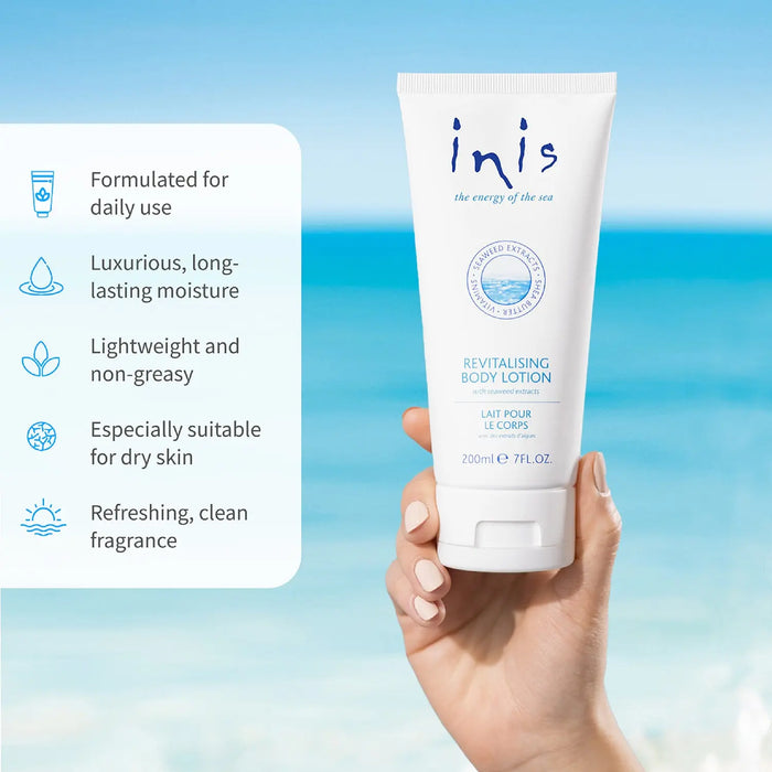 A hand holds a white tube of inis Revitalising Body Lotion against a tropical beach background