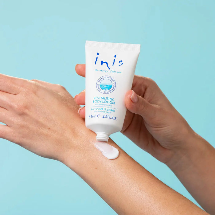 Person applying lotion from a 'inis' tube on a blue background