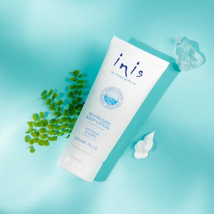 Inis revitalising body lotion on a light blue background with green leaves and a crystal.