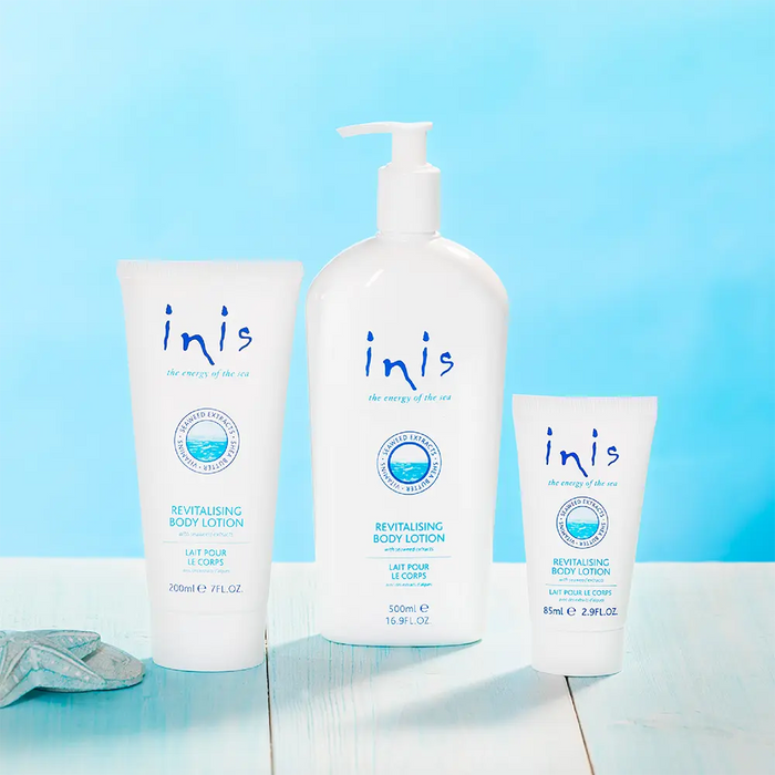 Three Inis body care products arranged on a light blue wooden surface against a bright blue background: a large body lotion bottle pump, a medium body lotion tube, and a smaller body lotion tube