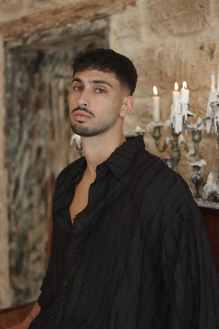 Man wearing a black RIPS Short Sleeve Button-Up Shirt with textured fabric, standing in front of a stone wall with lit candles