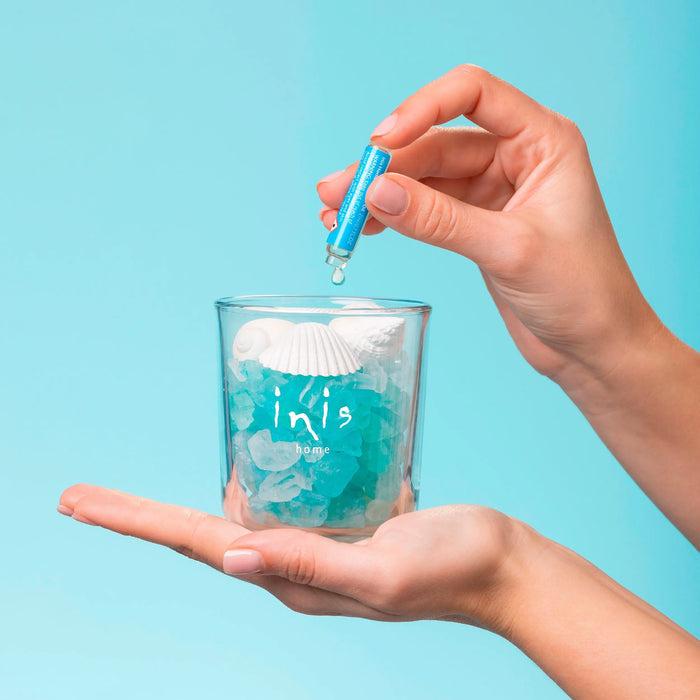 Hand pouring a blue liquid into a glass against a light blue background