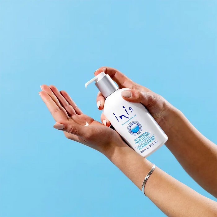 Person holding a bottle of 'inis' hand lotion product against a blue background