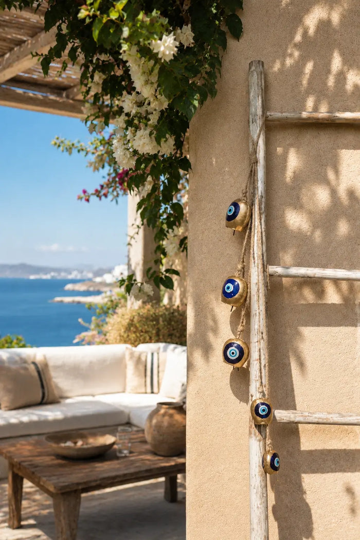 Graduated Bell Mobile (Large to Small) hanging on a wooden ladder against a beige wall, with a patio and ocean in the background