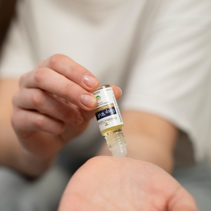 Person applying Sleep Well roll-on remedy to their wrist in a close-up with a blurred neutral background