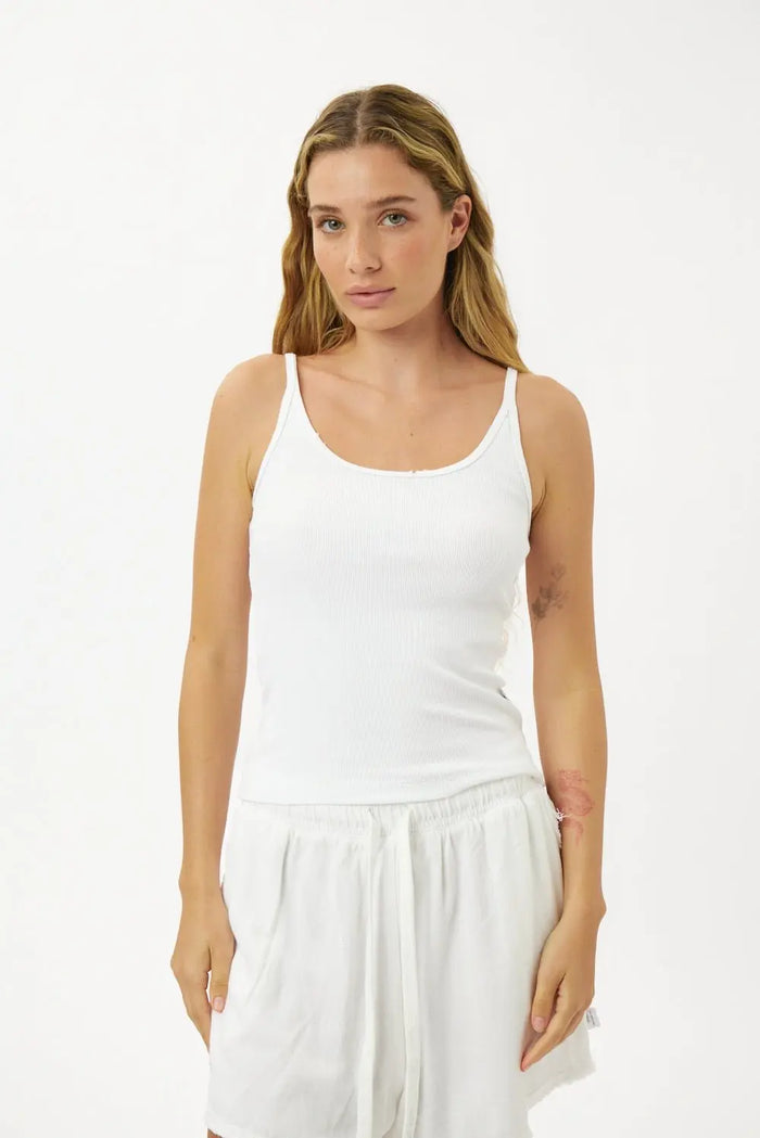 Woman wearing a white tank top and white pants on a white background