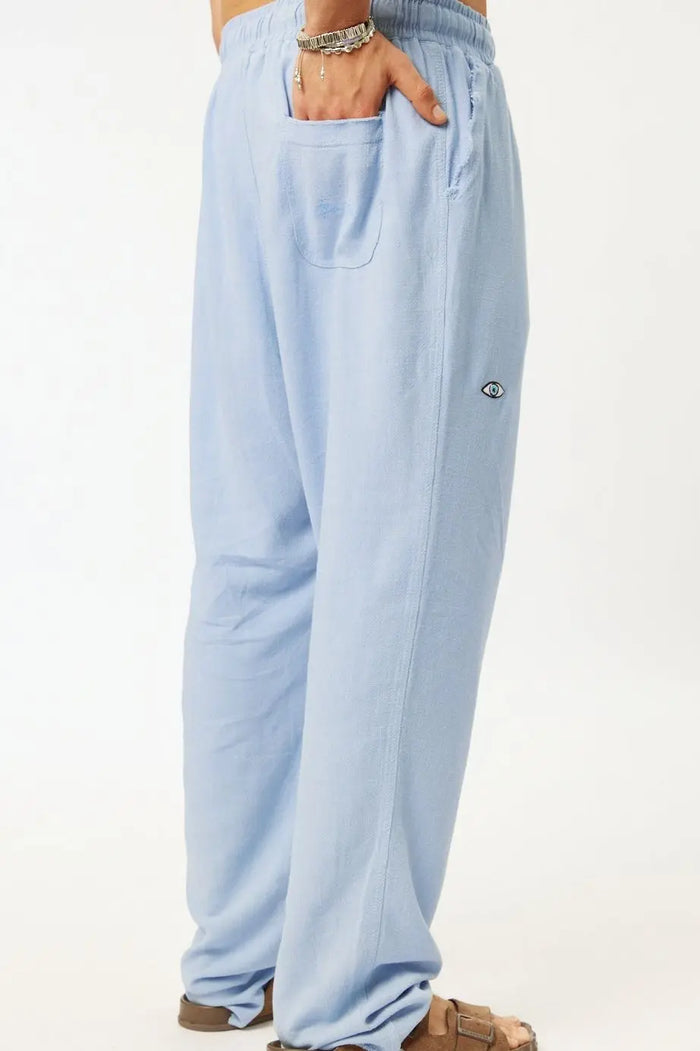SOFT SL Linen Pants in sky blue, with a hand in the back pocket and an eye logo on the side
