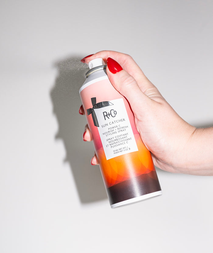 Hand holding a R+Co hair product can against a neutral background